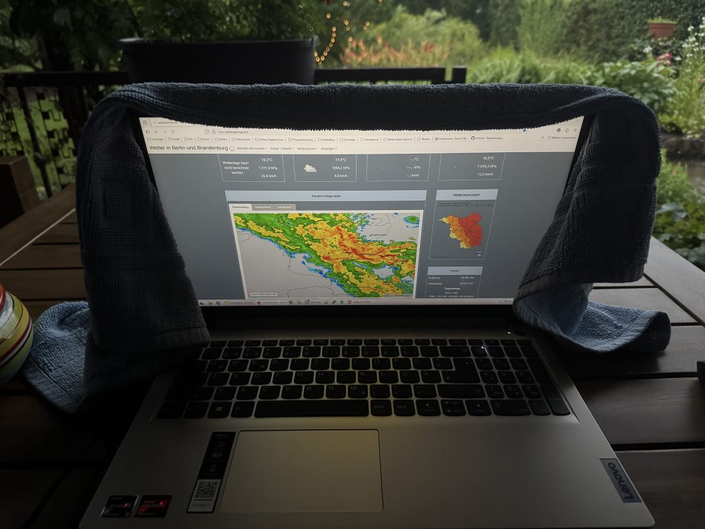 Laptop mit Handtuch vor Nässe geschützt, während man das Regenradar beobachtet